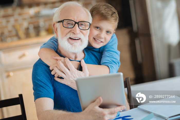 My family. Joyful nice happy boy smiling and hugging his grandfather while standing behind him