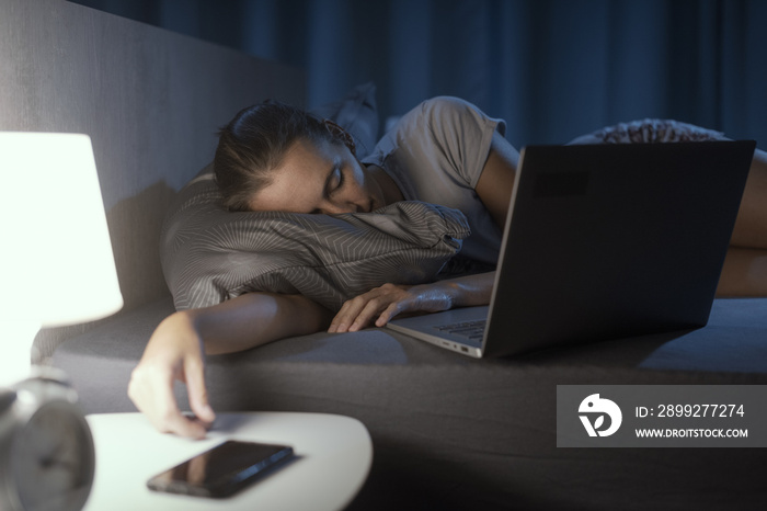 Woman falling asleep in front of her laptop in bed