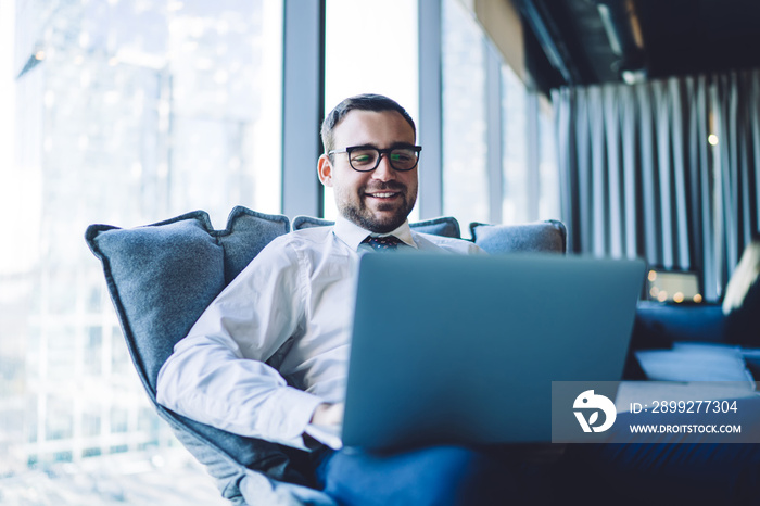 Happy smiling businessman having online conference via laptop computer sitting in office chair, cheerful male employer in spectacles having video call via notebook connected to company wifi internet