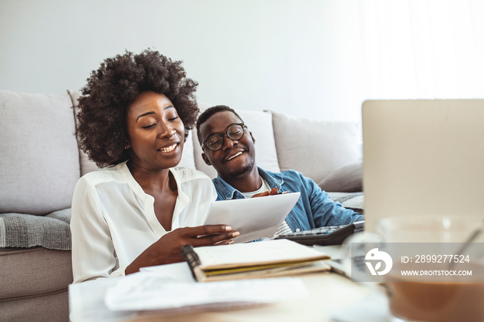 Happy couple with laptop spending time together at home. Happy young couple paying bills together and managing budget, sitting on the sofa and using calculator and laptop