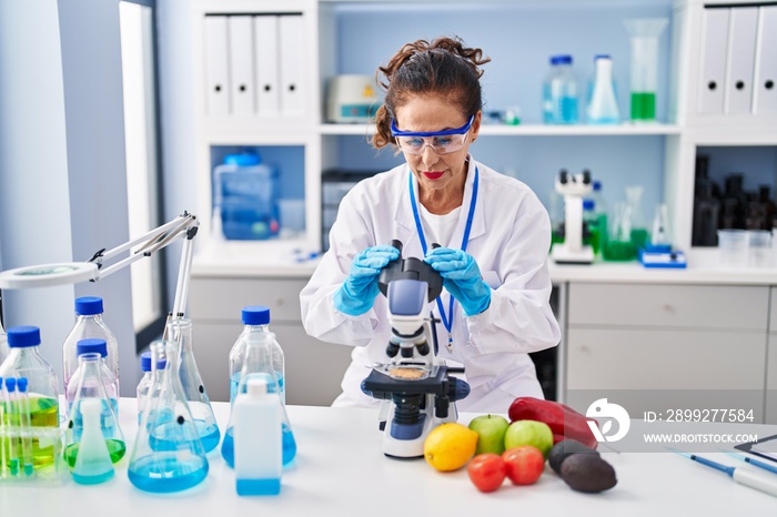 Middle age hispanic woman looking through microscope at laboratory