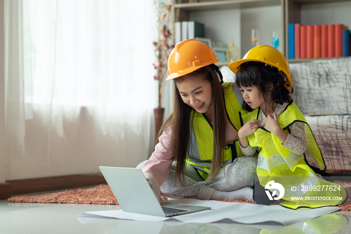 Little Asian girl engineer in yellow helmet using laptop with her mother, education and occupation concept