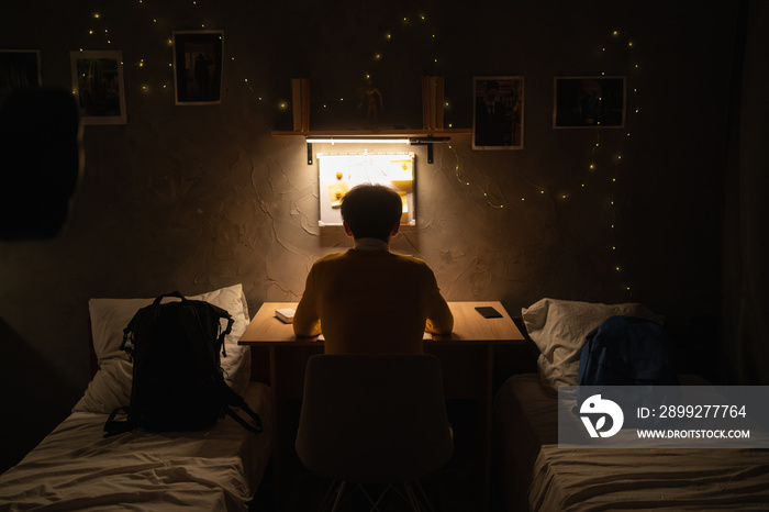 Late night study sessions. Back view of a young student studying late into the night in a dormitory.