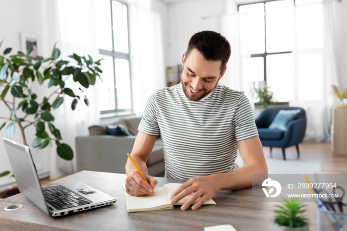 remote job, technology and people concept - young man with notebook and laptop computer working at home office