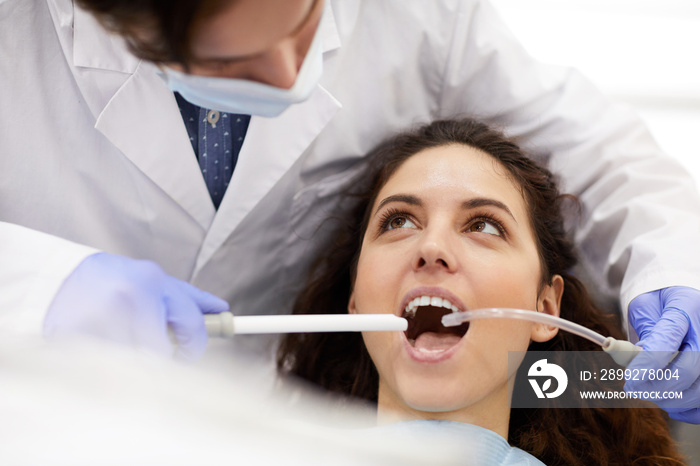 Head and shoulders portrait of beautiful young woman lying in dental chair with mouth open during treatment, copy space