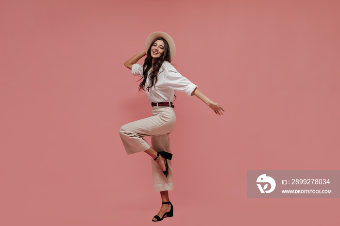 Pretty dark haired lady in black heels, stylish pants and long sleeve shirt looking into camera and smiling on isolated background..