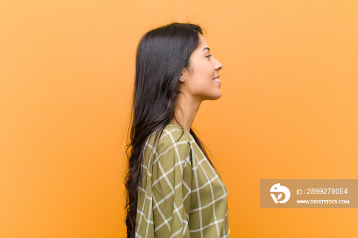 young pretty hispanic woman on profile view looking to copy space ahead, thinking, imagining or daydreaming against brown wall