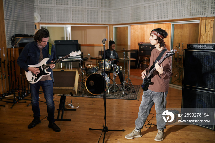 Full length portrait of alternative music band playing instruments in professional recording studio