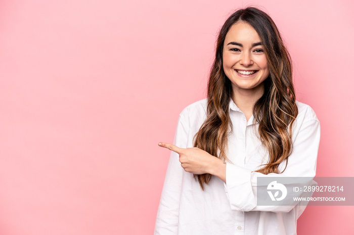 Young caucasian woman isolated on pink background smiling and pointing aside, showing something at blank space.