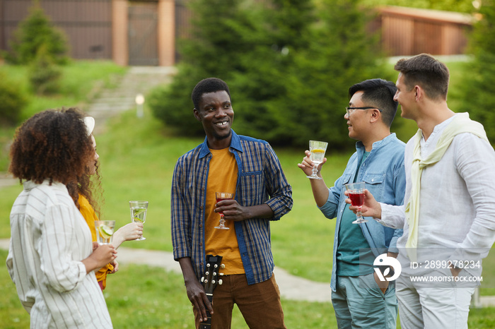 Multi-ethnic group of people drinking cocktails and chatting while enjoying outdoor party in Summer, copy space