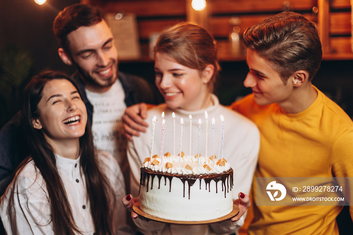 Portrait of joyful girl holding birthday cake surrounded by friends who came to rejoice and congratulate their girlfriend on her birthday