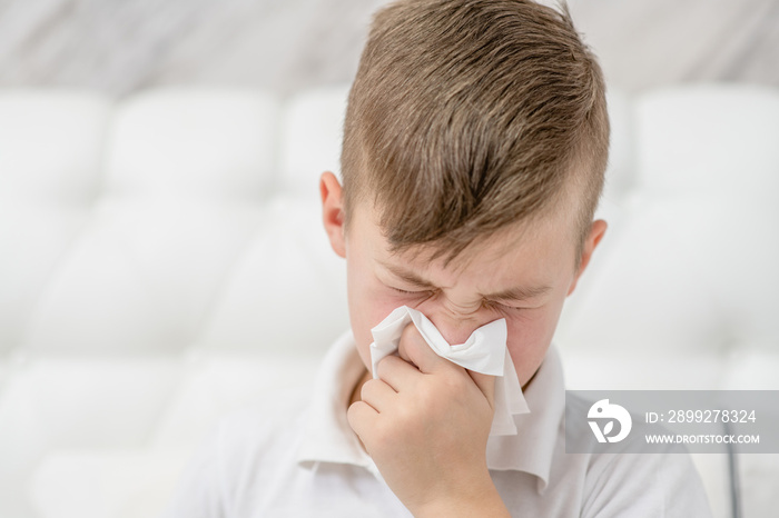 Sick child on bed blowing his nose in tissue. Empty space for text