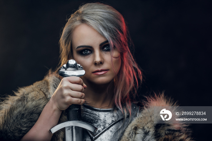 Portrait of a beautiful warrior woman holding a sword wearing steel cuirass and fur. Fantasy fashion. Studio photography on a dark background. Cosplayer as Ciri from The Witcher.