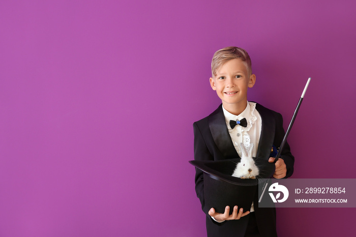 Cute little magician holding hat with rabbit on color background