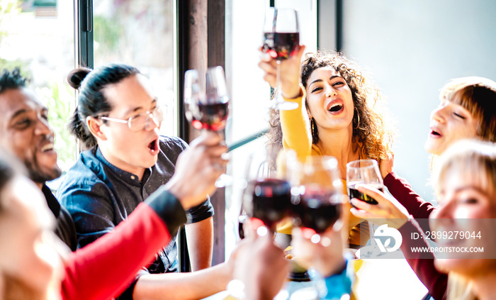 Young multicultural friends drinking and toasting red wine at dinner party - Happy drunk people having fun together at restaurant winery bar - Dinning life style concept on bright vivid filter