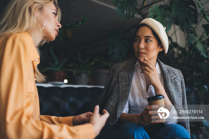 Caucaisan and Asian women in trendy outfits discussing business ideas during coffee break for live socializing, attractive diverse hipster girls with takeaway cup talking about fashion style