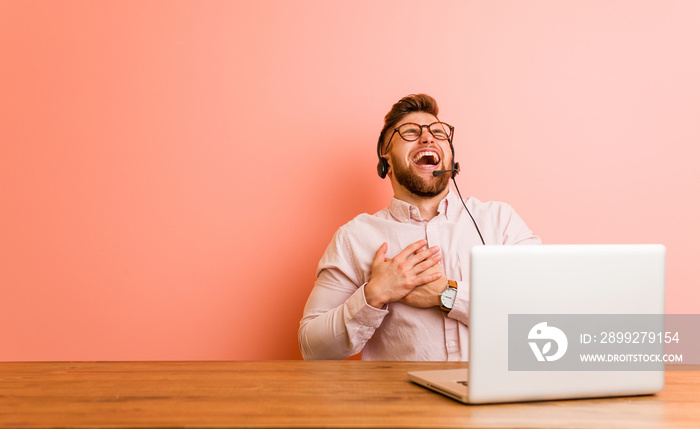 Young man working in a call center laughing keeping hands on heart, concept of happiness.