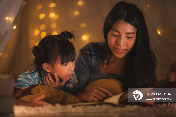 young Asian mother read the story in the book for her daughter children on the bed at home, family and motherhood learning concept