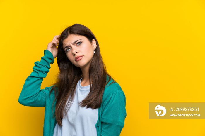 Teenager girl over yellow wall having doubts and with confuse face expression