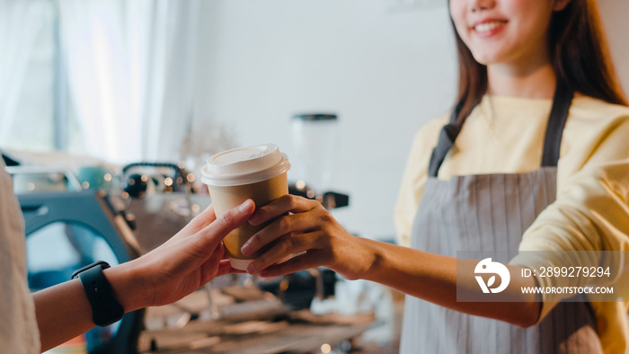 Young Asia female barista serving take away hot coffee paper cup to consumer standing behind bar counter at cafe restaurant. Owner small business, food and drink, service mind concept.