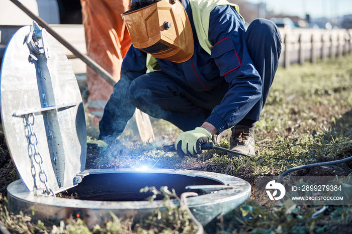 Welder handyman working on a sewer manhole lid.