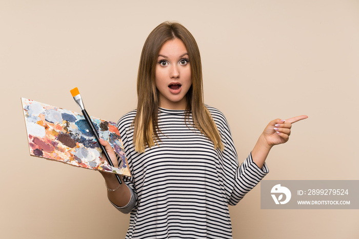 Teenager girl holding a palette over isolated background surprised and pointing finger to the side