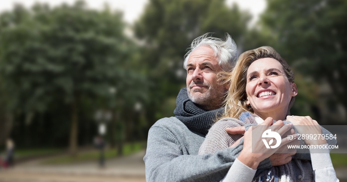 Smiling caucasian senior man embracing senior woman against trees in park during sunny day