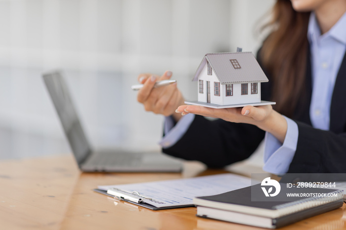 Wooden toy house with real estate agent Asian business woman signs a purchase contract mortgagefor rent sell insurance or loan for a home, Real estate concept.