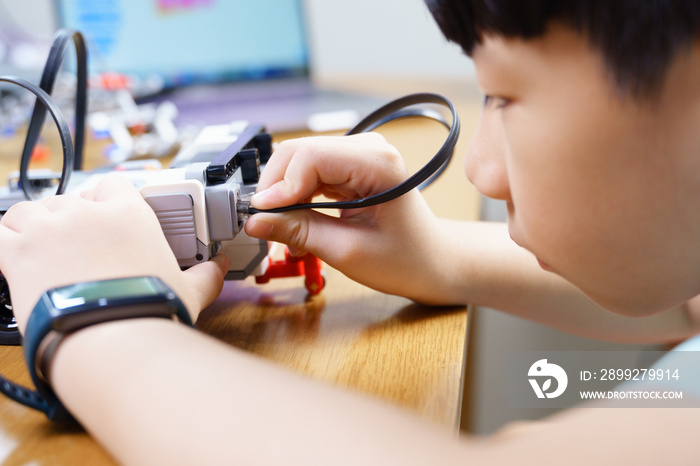 Close up of Asian student child’s hands and face connecting cable  to vehicle robot, testing and solving engineering problem on table. STEM education and 21st century learning skills concept