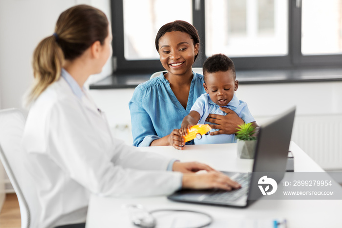 medicine, healthcare and pediatry concept - happy african american mother with baby son and caucasian doctor with laptop computer at clinic