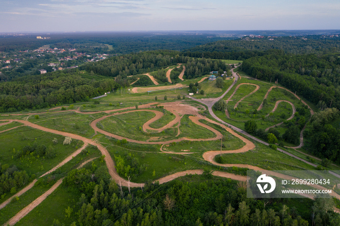 Location with several off-road motorcycle tracks for competitions and training. Dirt track with hills and trees. Panoramic Drone Shot.