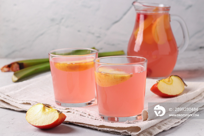 Compote of rhubarb, apples and cherries in two glasses and a jug on light gray background