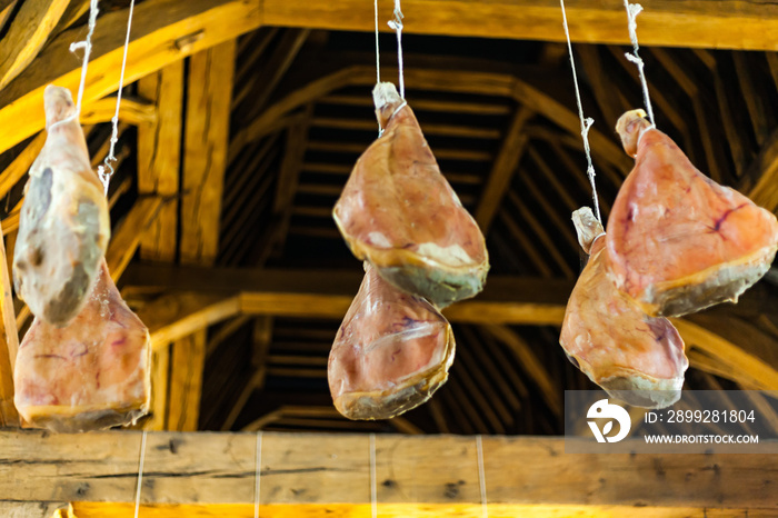 Hooked ham on wooden beams that hang from the ceiling. Traditional way of drying meat. Pork ham drying on the air