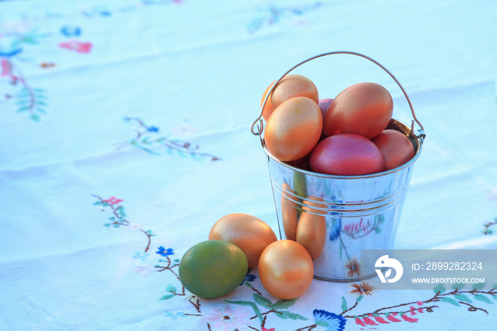 A galvanized bucket full of painted Easter eggs against the background of a snow-white Ukrainian towel embroidered with flowers