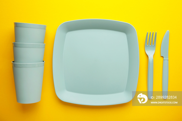 Bright plastic disposable tableware on yellow background.