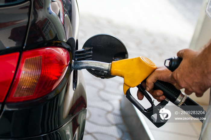 Pumping gas at gas pump. Closeup of man pumping gasoline fuel in car at gas station. Man’s hand refueling car at gas station. Gas pump nozzle in the fuel tank