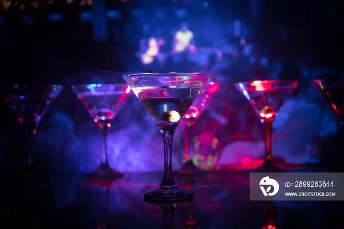 Several glasses of famous cocktail Martini, shot at a bar with dark toned foggy background and disco lights. Club drink concept