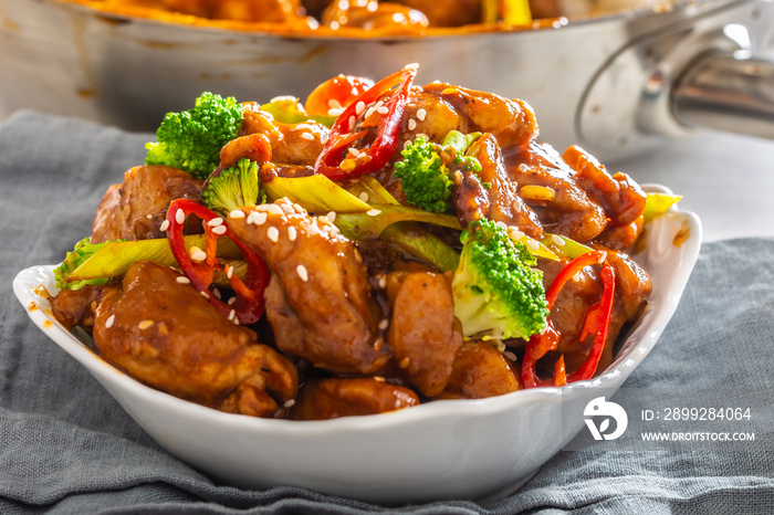 Bowl of teriyaki chicken sprinkled with seesame seeds, fresh chillies and broccoli