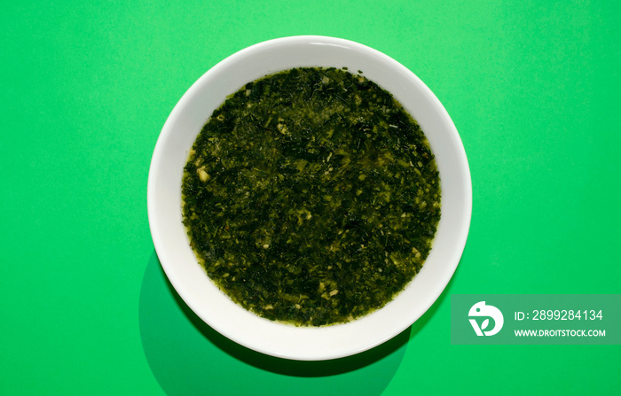 Famous traditional Arabic cuisine. Molokhia soup in a white bowl on a green background. Flat lay, top view