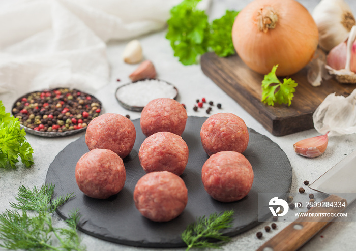 Fresh beef meatballs on stone board with pepper, salt and garlic on light background with dill,parsley and dill.