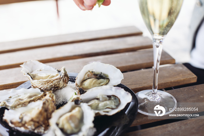 Squeezing lime on oysters. Two glasses of sparkling wine on a wooden table in an outdoor cafe