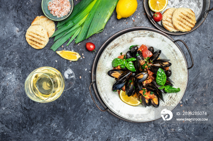 Fine dining in a seafood restaurant: a big dish of mussels with bottle of white wine with two wine glasses, on dark background. Restaurant menu, dieting, cookbook recipe top view