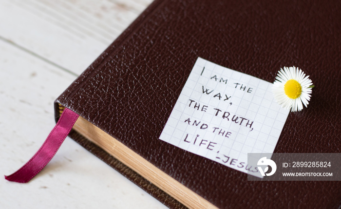 Jesus Christ is the Way, the Truth, and the Life. Handwritten text note on Holy Bible on a wooden background. Biblical concept of faith and hope.