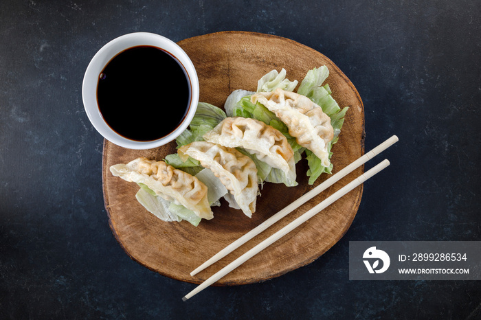 Gyozas served in black plate on wooden log, with chopsticks and black background