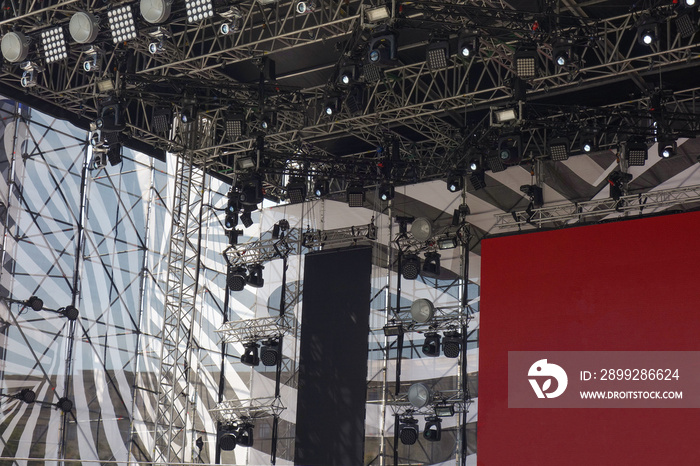 Stage for concert or show under blue sky. Light equipment with illuminated spot and LED lights. Sound and video equipment on metal frame construction installed outside