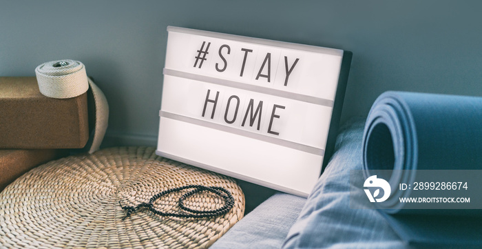 Coronavirus Yoga at home sign lightbox with text hashtag #STAYHOME glowing in light with exercise mat, cork blocks, strap meditation pillows. COVID-19 banner to promote self isolation staying at home.