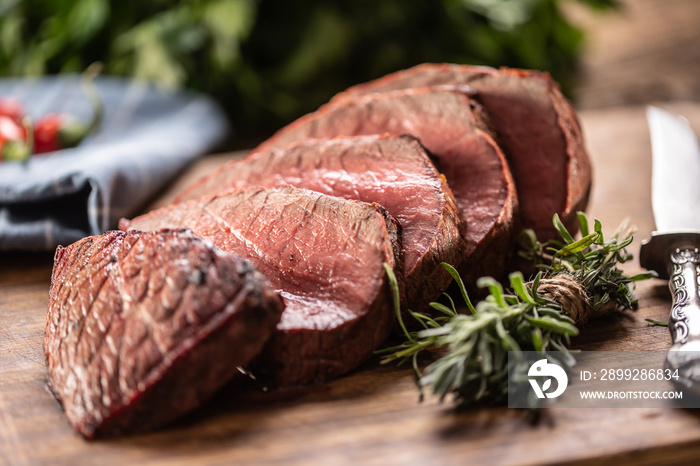 Rump steak cut to slices on a chopping board next to a knife and rosemary