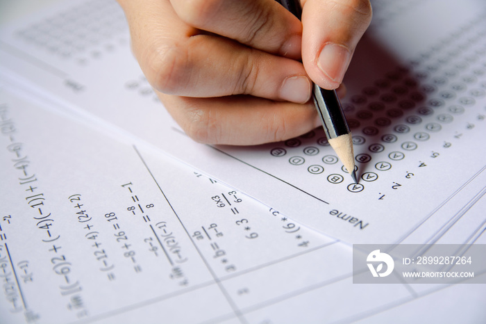 Exam. Students holding pencil writing selected choice on answer sheets and Mathematics question sheets. students testing doing examination. school exam