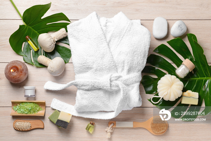 Clean bathrobe with spa supplies on wooden background