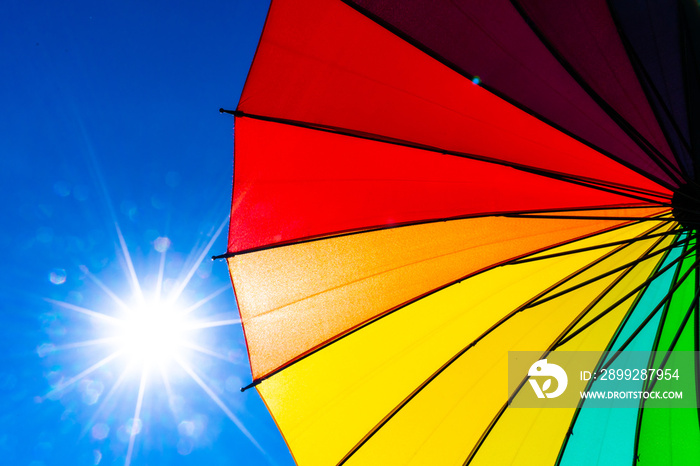 Multicolored of rainbow umbrella in bottom view for protect skin from the sun, high uv on the blue summer sky with white fluffy clound. Freedom in the blue sky.